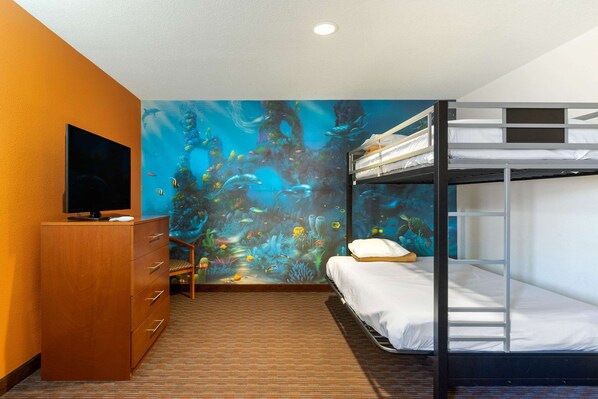 A hotel room with a bunk bed, a wooden dresser, a flat-screen TV, and an ocean-themed mural on the wall.