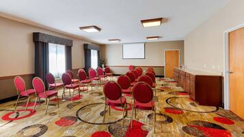 A conference room with rows of red chairs, a projector screen, and a carpet with circular patterns.