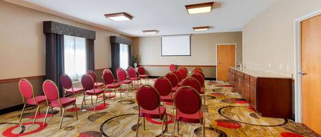 A conference room with rows of red chairs, a projector screen, and a carpet with circular patterns.