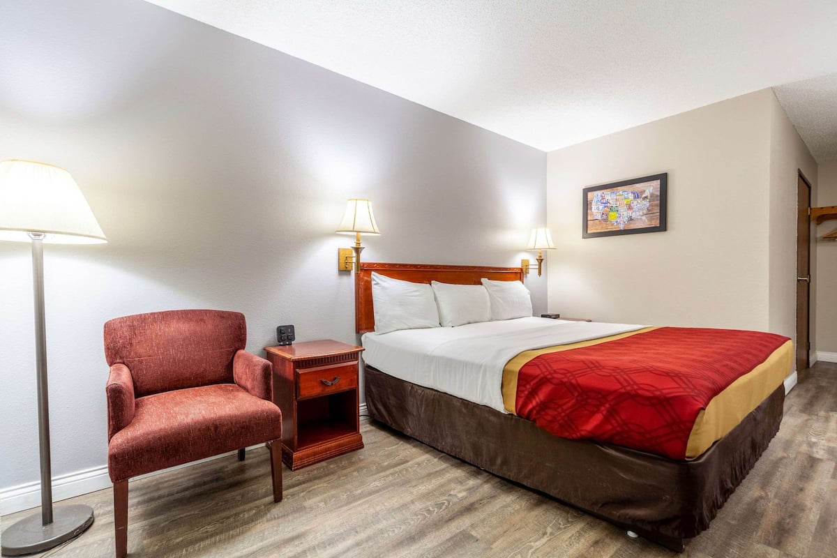 A hotel room with a bed, a chair, a nightstand, and two wall-mounted lamps.