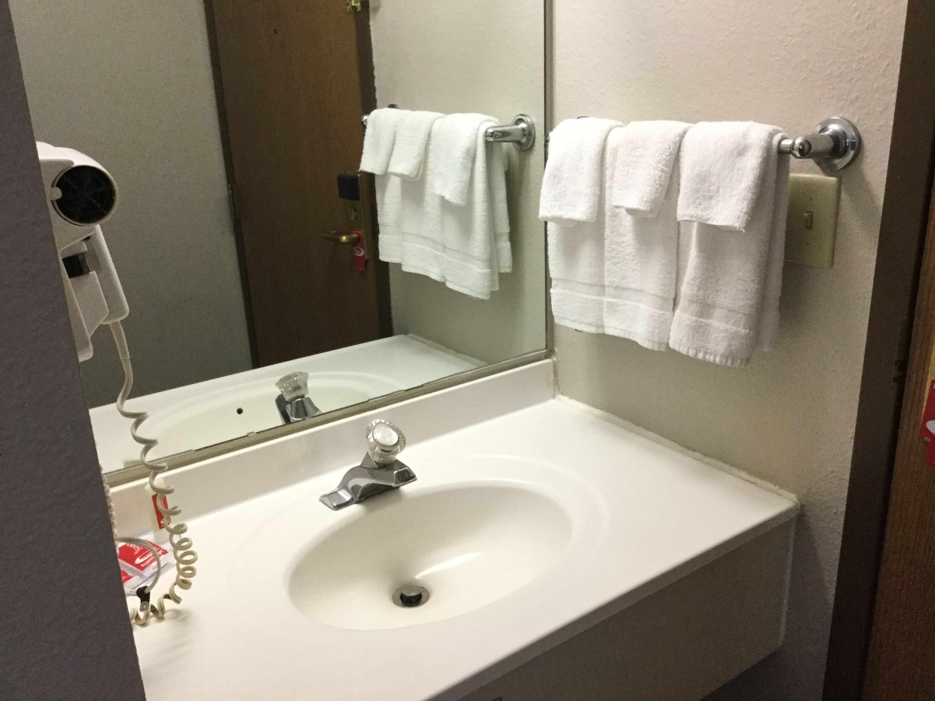 A bathroom with a white sink, a mirror, and a towel rack with white towels.