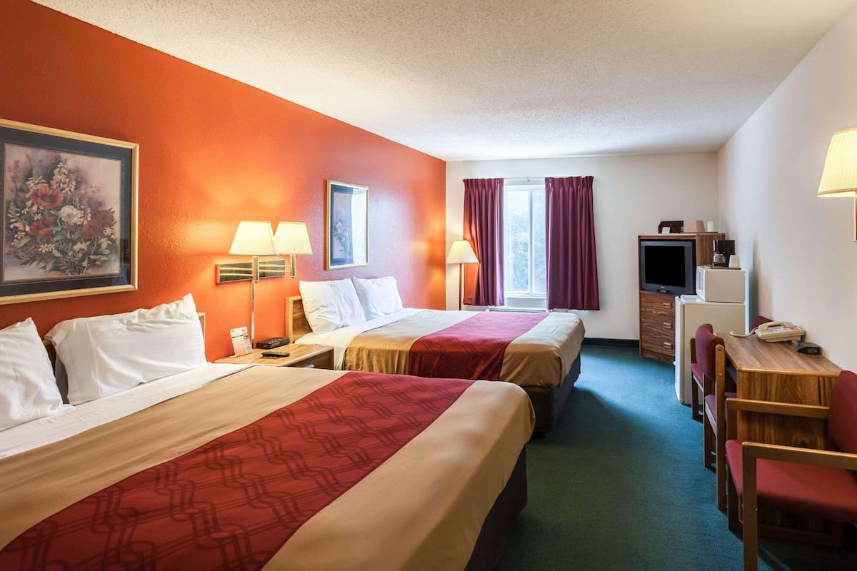 A hotel room with two beds, a desk, a television, and a window with curtains.
