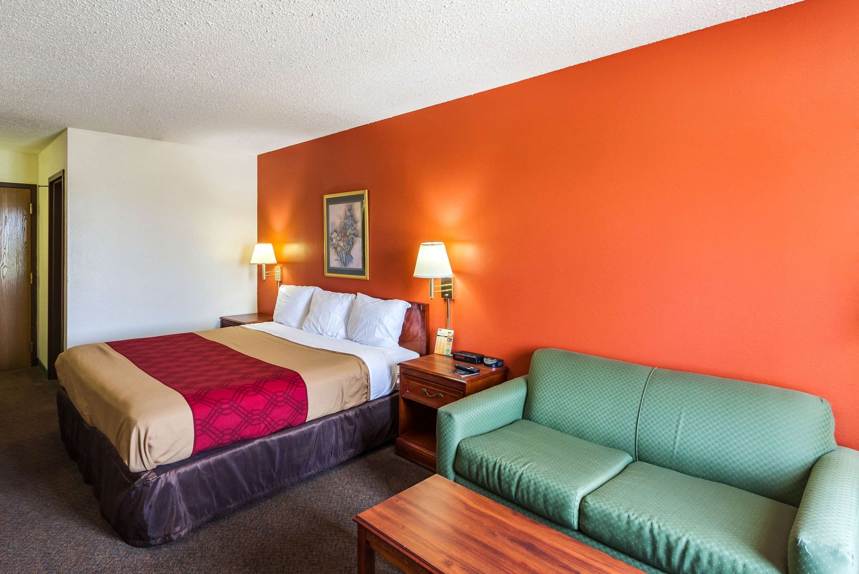 A hotel room with a bed, a green sofa, and two bedside lamps.