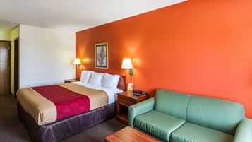 A hotel room with a bed, a green sofa, and two bedside lamps.