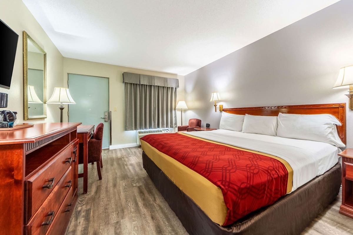 A hotel room with a bed, a desk, a chair, a mirror, and a window with curtains.