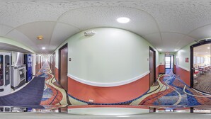 A corridor with vending machines, a carpeted floor, and a door leading to a room with a table and chairs. - Econo Lodge Lincoln (Lincoln)
