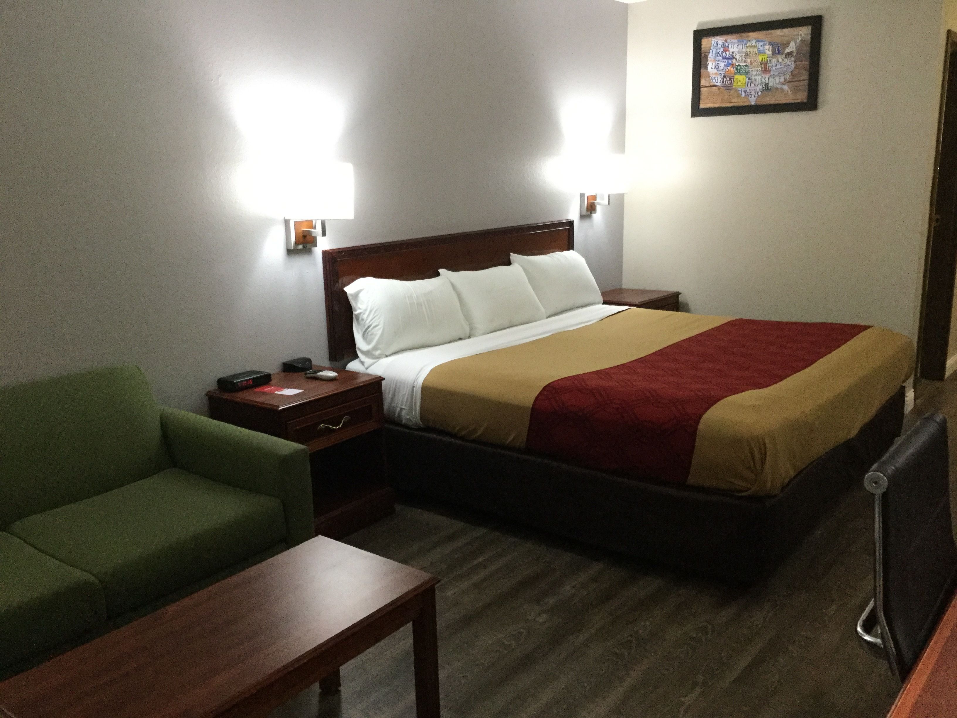 A hotel room with a bed, a green armchair, a wooden nightstand, and a desk.