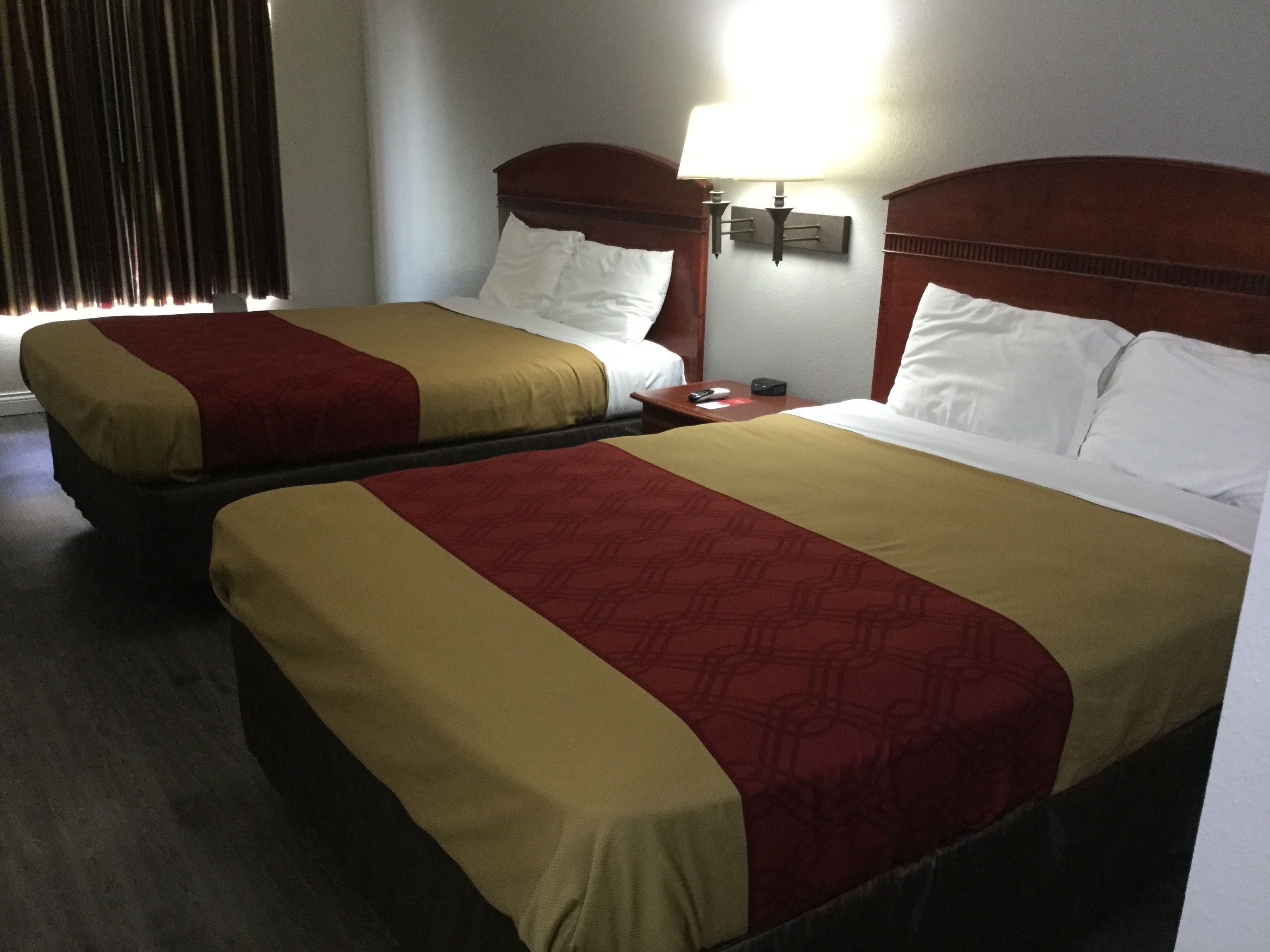Two adjacent beds with wooden headboards, a bedside table with a lamp, and a window with curtains.