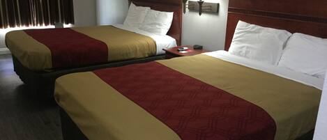 Two adjacent beds with wooden headboards, a bedside table with a lamp, and a window with curtains.