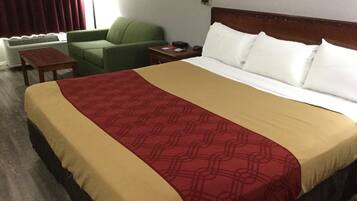 Quarto de hotel com uma cama grande, uma poltrona verde, uma mesinha e um criado-mudo com abajur.
