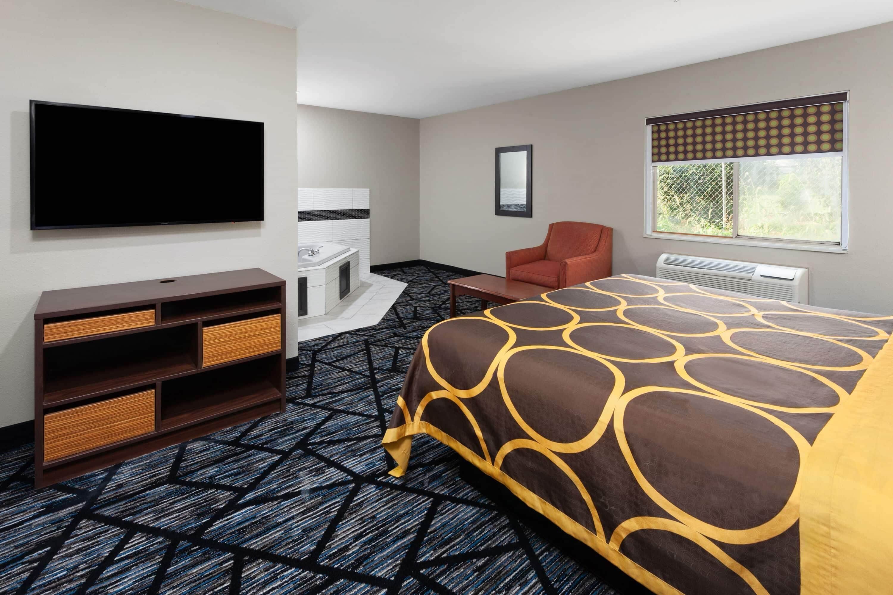 A hotel room with a bed, a TV, a chair, a desk, a bathroom, and a window.