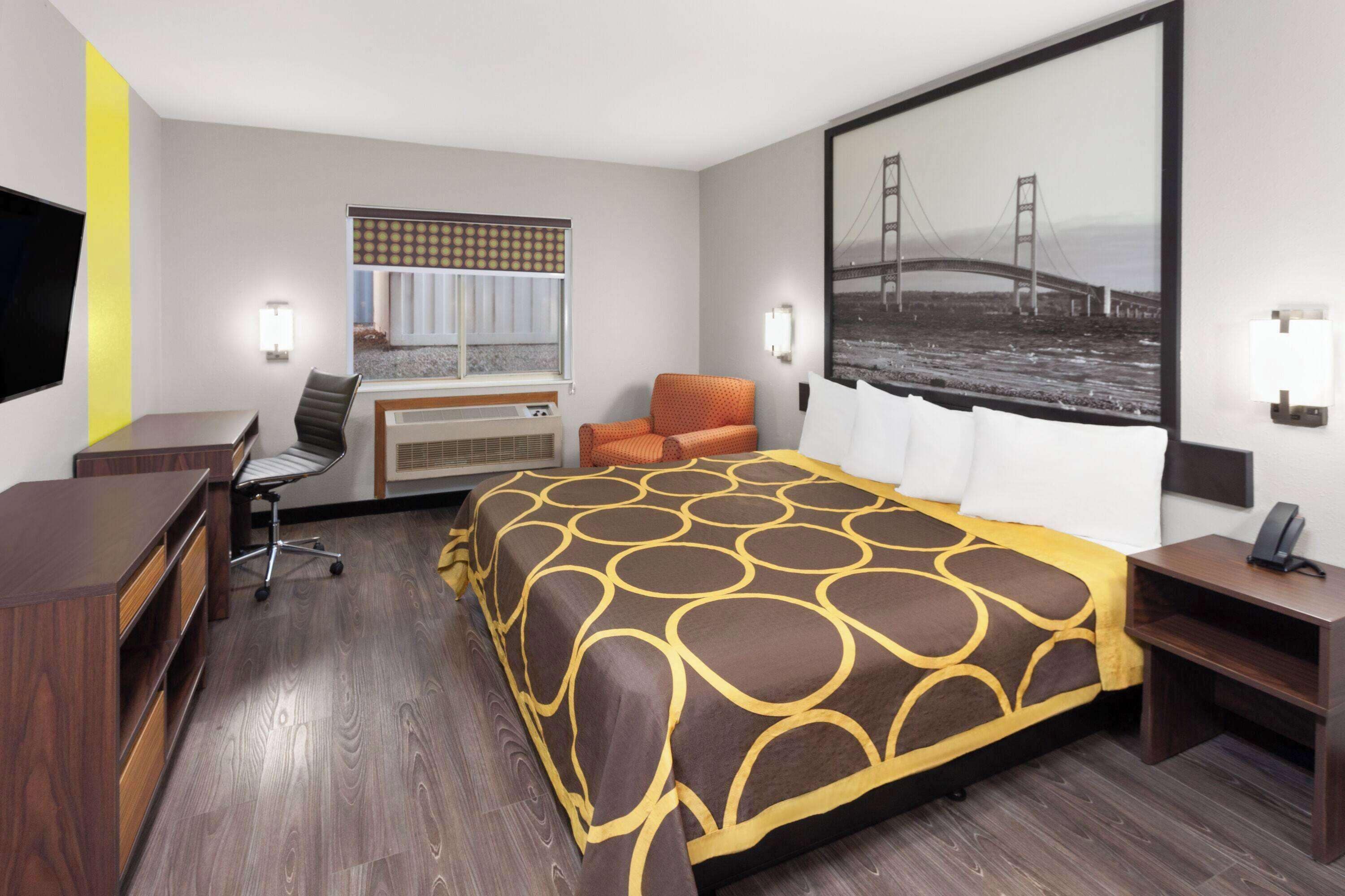 A hotel room with a bed, desk, chair, and a large window with a view of a bridge.