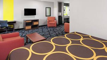 Habitación de hotel con cama, dos sillones rojos, una mesita, televisor, microondas y baño visible a través de una puerta abierta.
