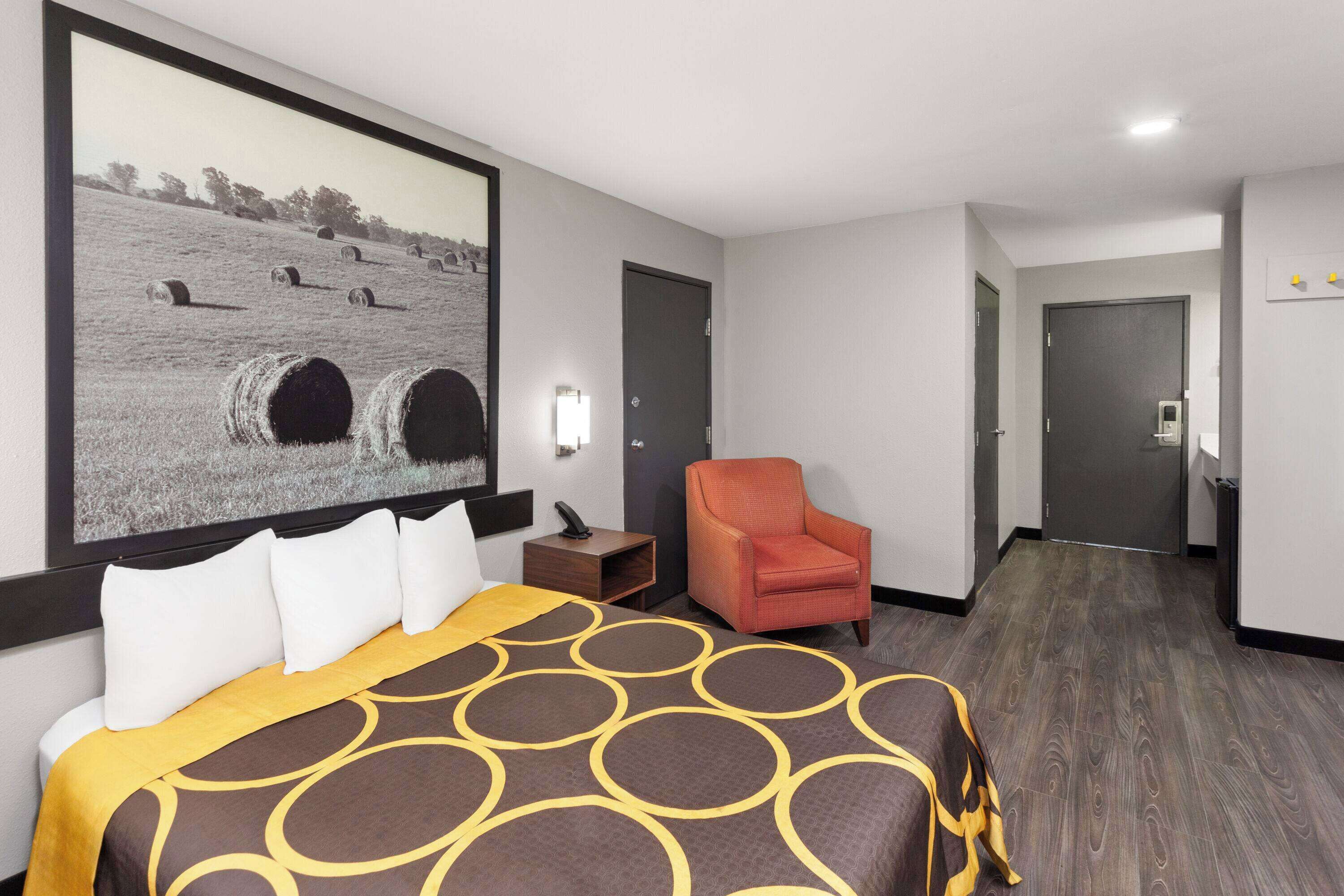 Habitación de hotel con una cama grande, un sillón naranja, un cuadro de pacas de heno y suelo de madera.