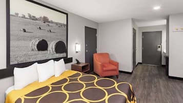 Habitación de hotel con una cama grande, un sillón naranja, un cuadro de pacas de heno y suelo de madera.
