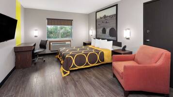 Habitación de hotel con cama, escritorio, silla, televisor, ventana con persianas, un cuadro y una puerta.