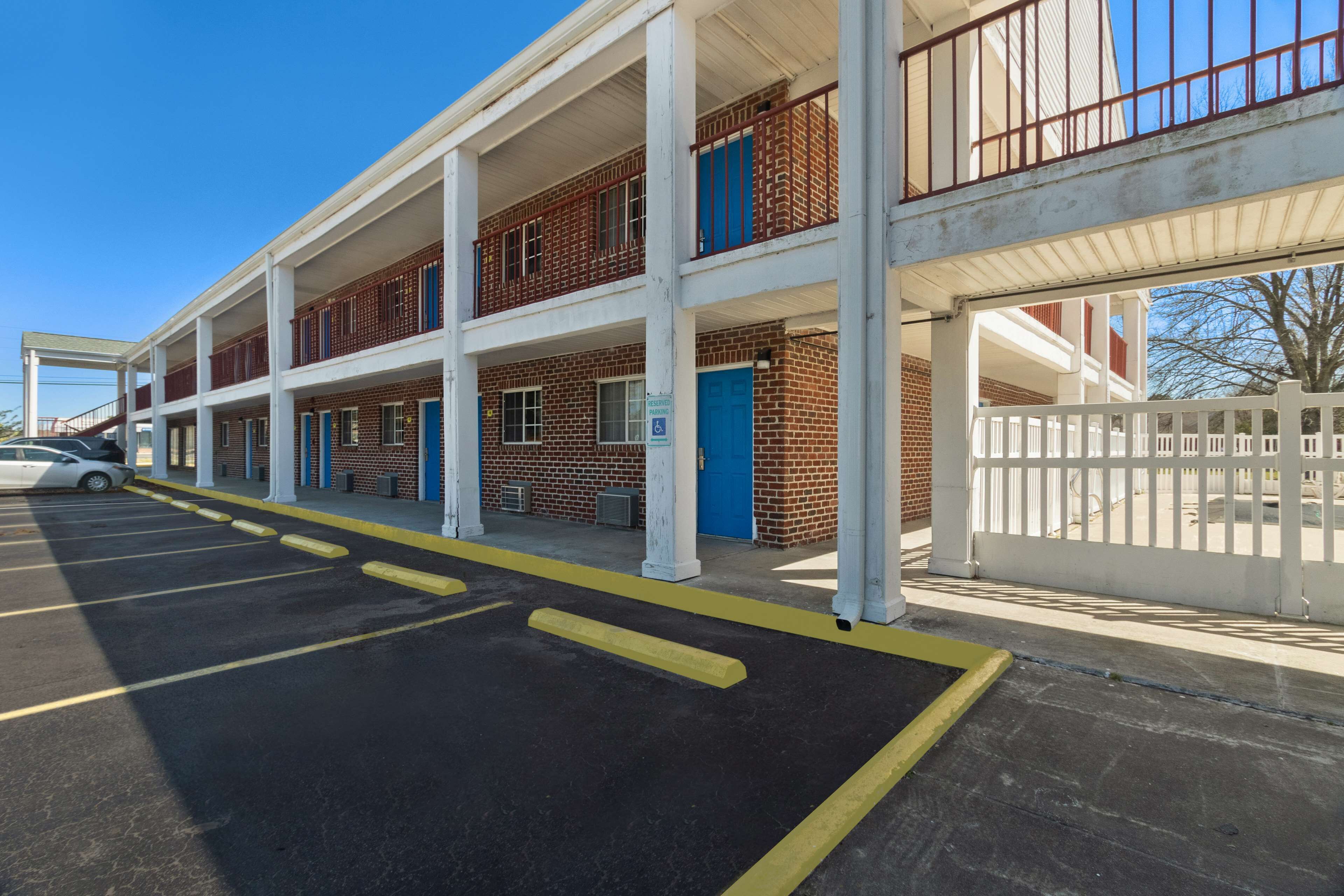 A multi-story building with a parking lot, a white fence, and a blue door.