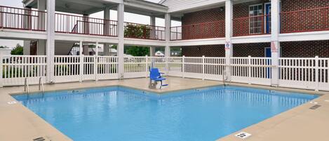 A pool area with a white fence, a blue chair, and a no diving sign.