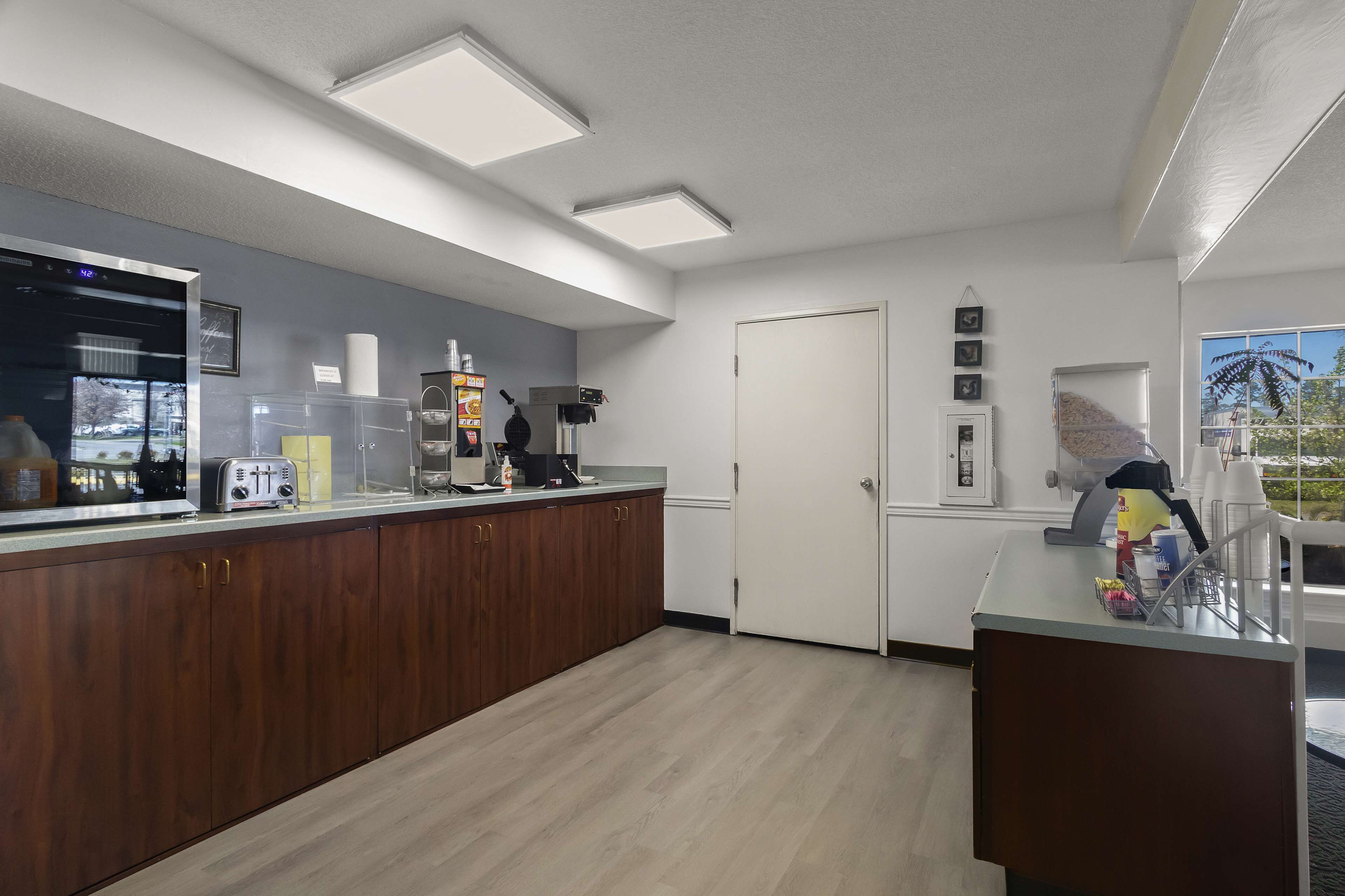 A modern kitchen with wooden cabinets, a built-in coffee machine, and a large window offering a view of the outdoors.