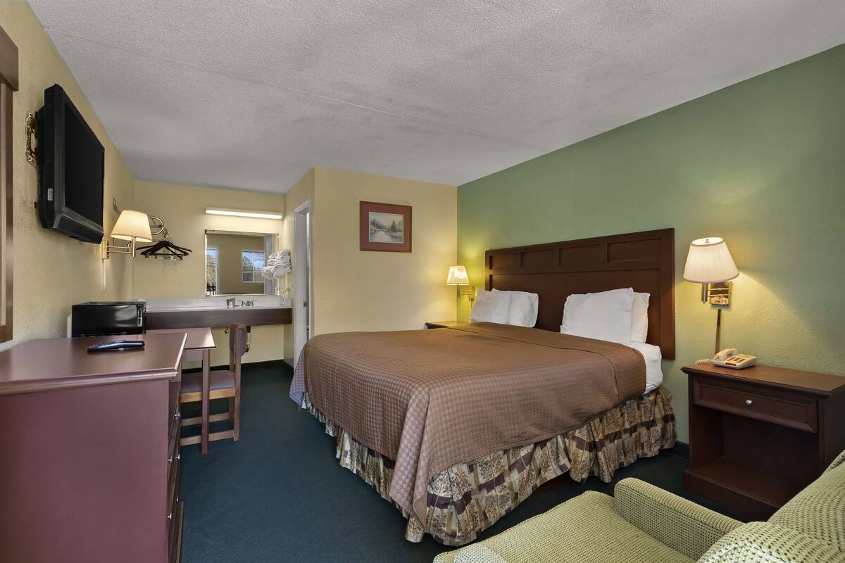 A hotel room with a bed, desk, chair, and a television mounted on the wall.