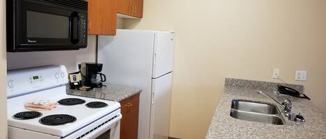 A kitchen with wooden cabinets, a white refrigerator, a microwave, a stove, and a granite countertop with a sink.