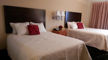 A hotel room with two beds, each with a dark headboard, white linens, and red pillows. There is a nightstand with a lamp and a phone.