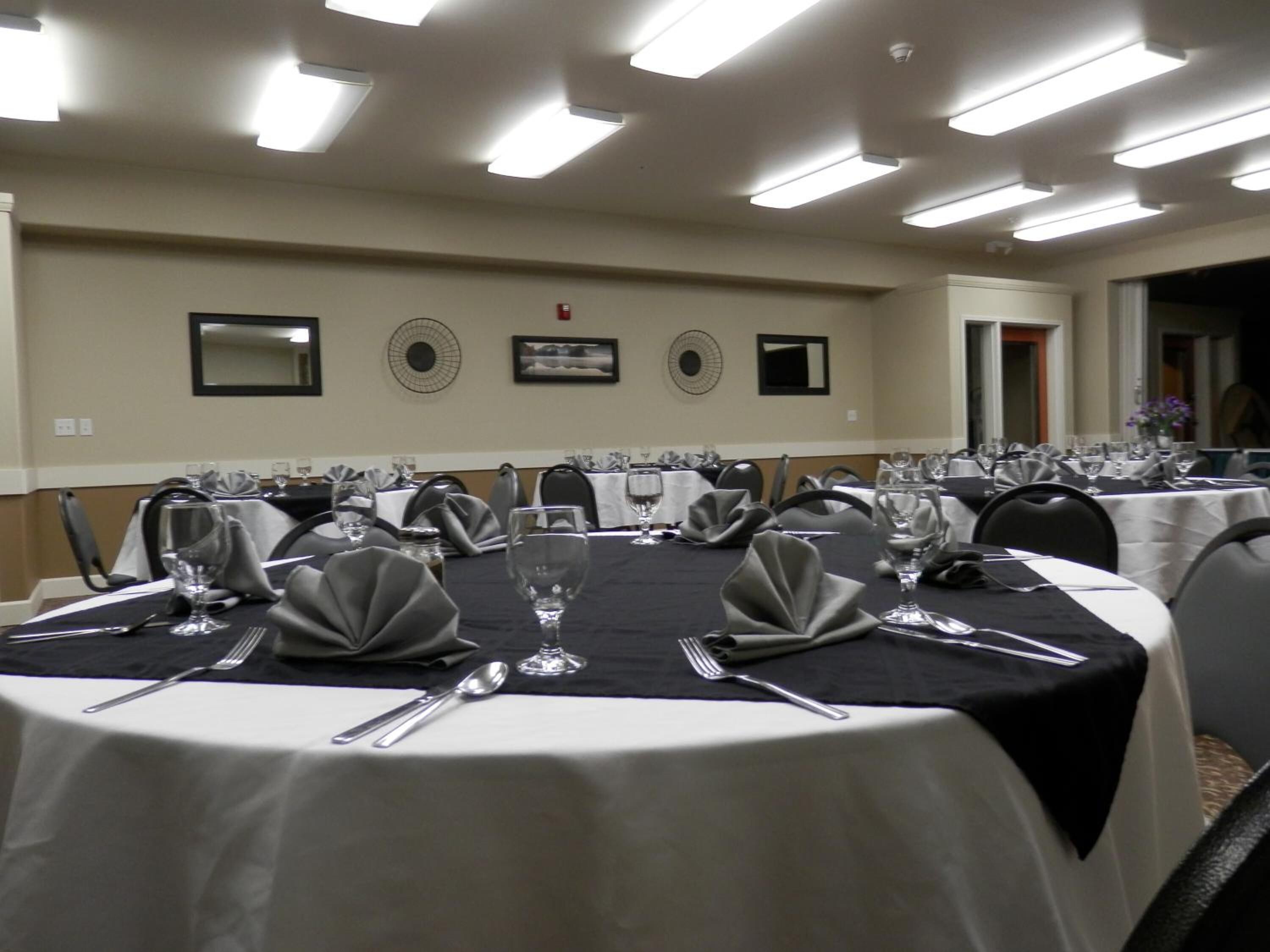 A conference room with round tables, each set with cutlery, glasses, and napkins.