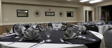 A conference room with round tables, each set with cutlery, glasses, and napkins.