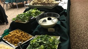 Een buffet met verschillende gerechten, waaronder Caesar salade, croutons, geraspte kaas en een bakje dip.