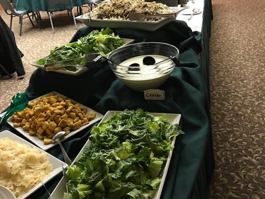 A buffet table with various food items including Caesar salad, croutons, shredded cheese, and a bowl of dip.
