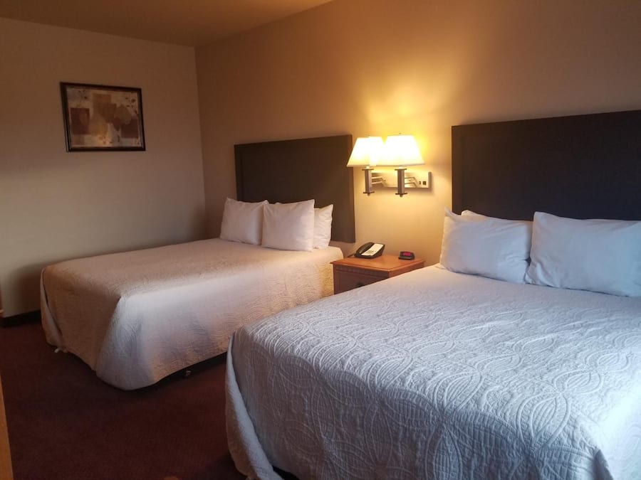 Habitación de hotel con dos camas, una mesita de noche con lámpara y un cuadro en la pared.