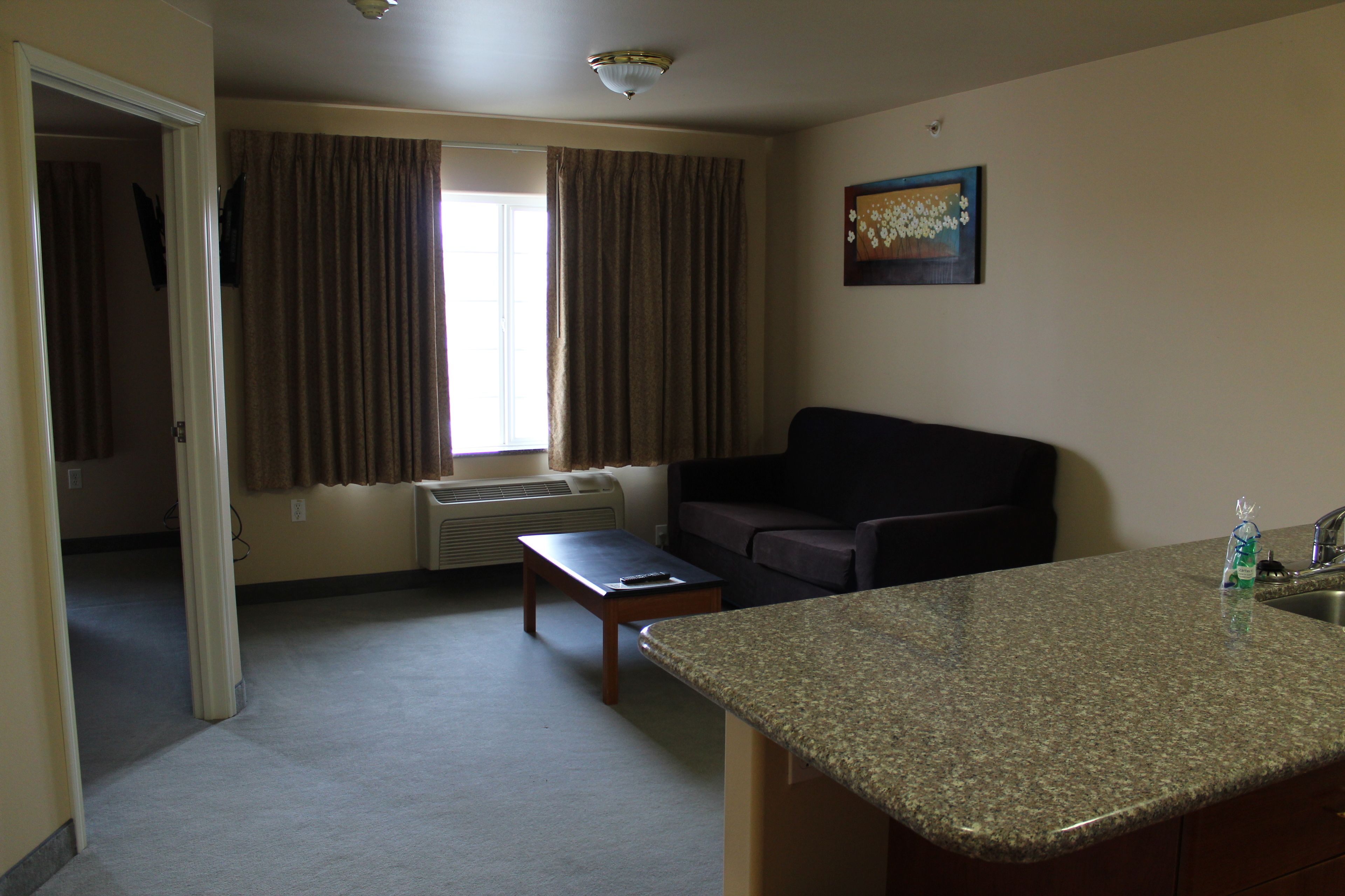 A compact living space with a kitchenette, a sofa, a small table, and a window with curtains.