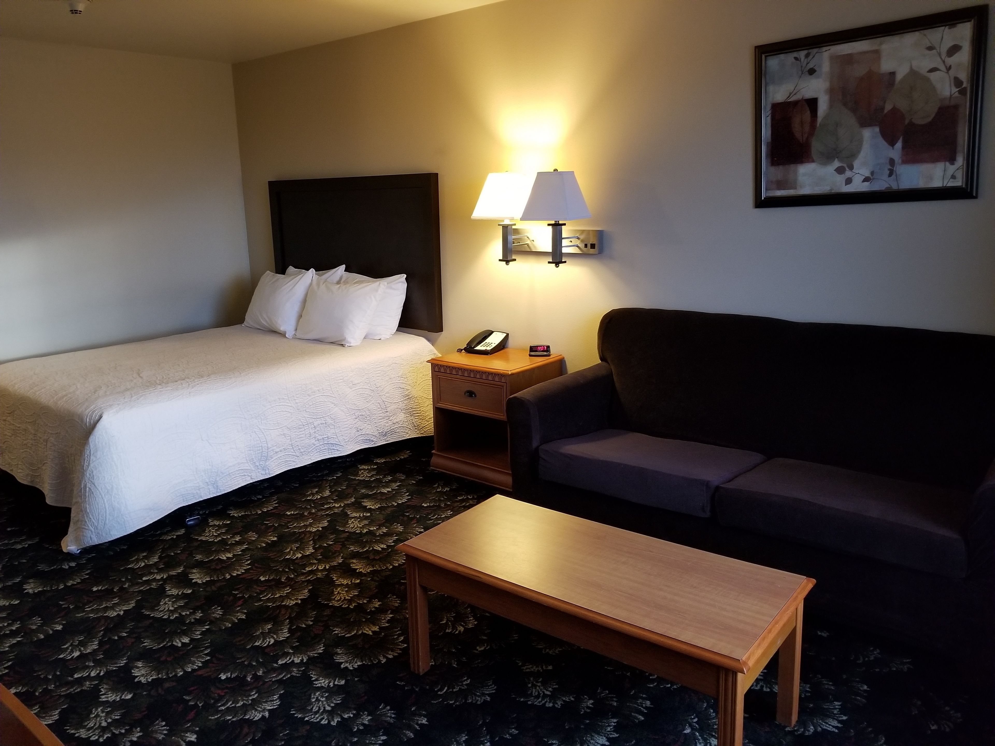 Quarto de hotel com cama, mesa de cabeceira, luminária, sofá e uma pequena mesa.