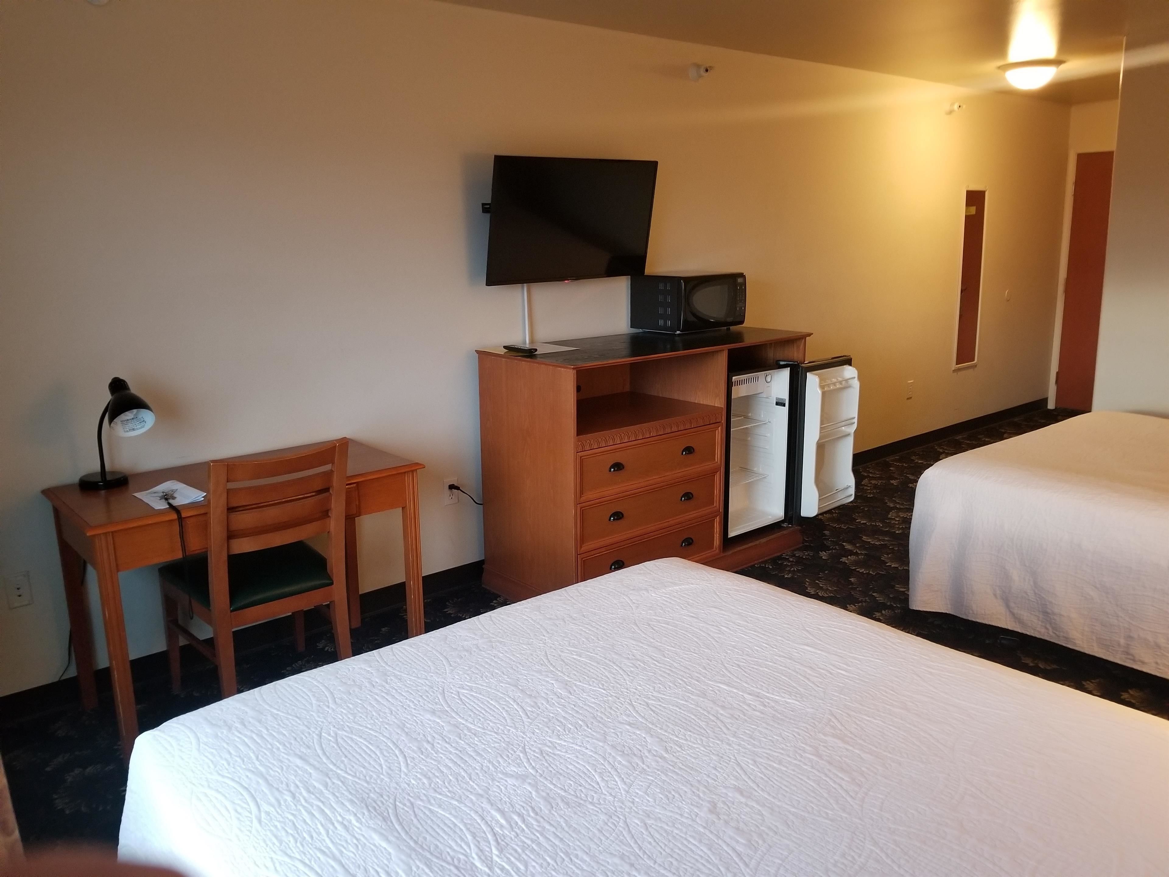 Habitación de hotel con dos camas, un escritorio con silla, televisor, refrigerador y lámpara.