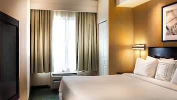 Habitación de hotel con cama, televisión, ventana con cortinas y lámpara fijada a la pared.