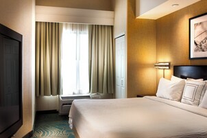 A hotel room with a bed, a television, a window with curtains, and a wall-mounted light fixture.