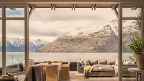 A spacious balcony with a view of snow-capped mountains and a lake. There are wicker chairs, a sofa, and a table with a bowl of fruit. - Rosewood Matakauri (Closeburn)