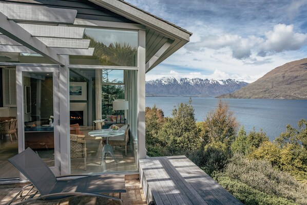 A modern house with a glass door leading to a patio with a lounge chair and a table.