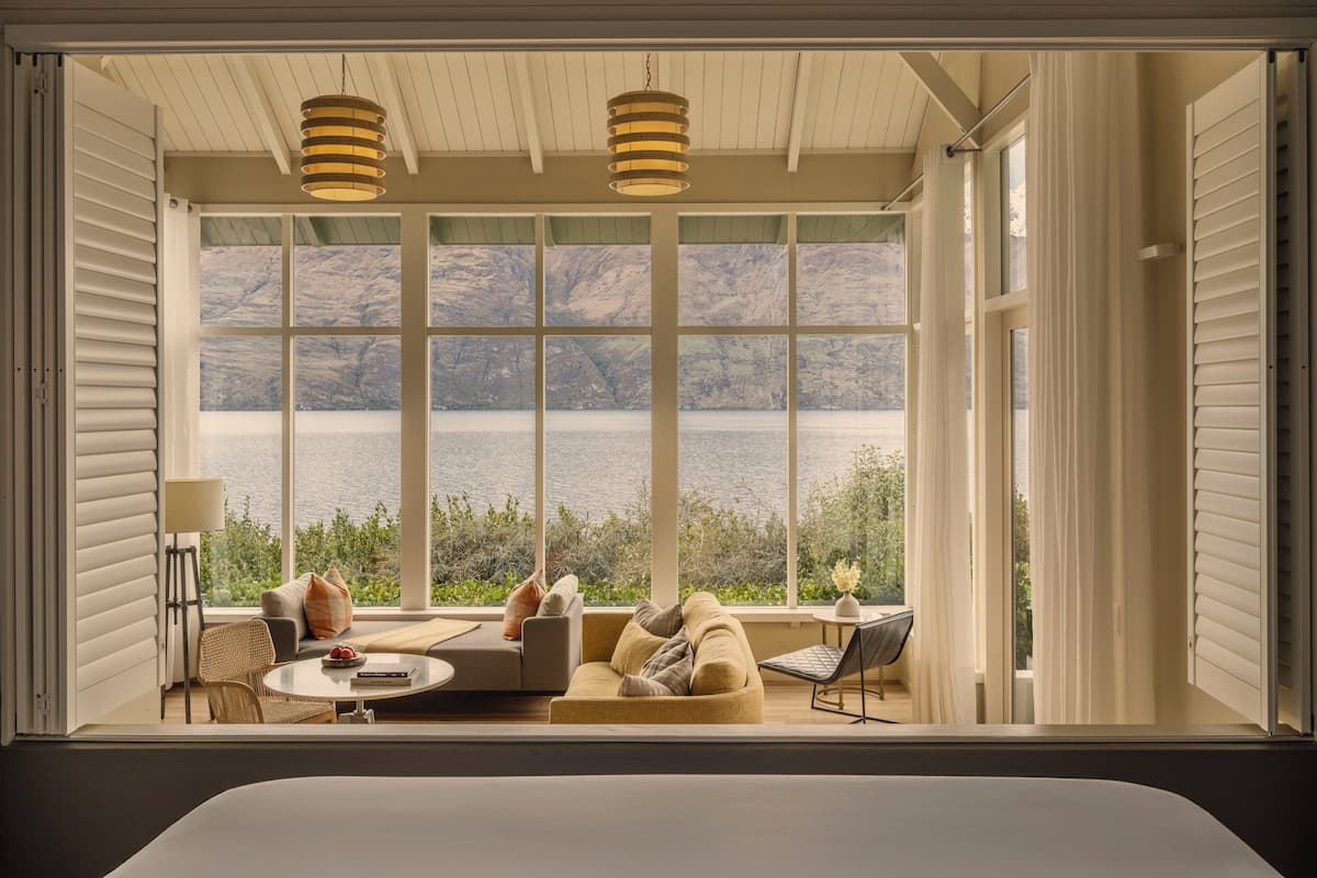 A room with a large window overlooking a lake, a sofa, a small table, and two hanging lamps.