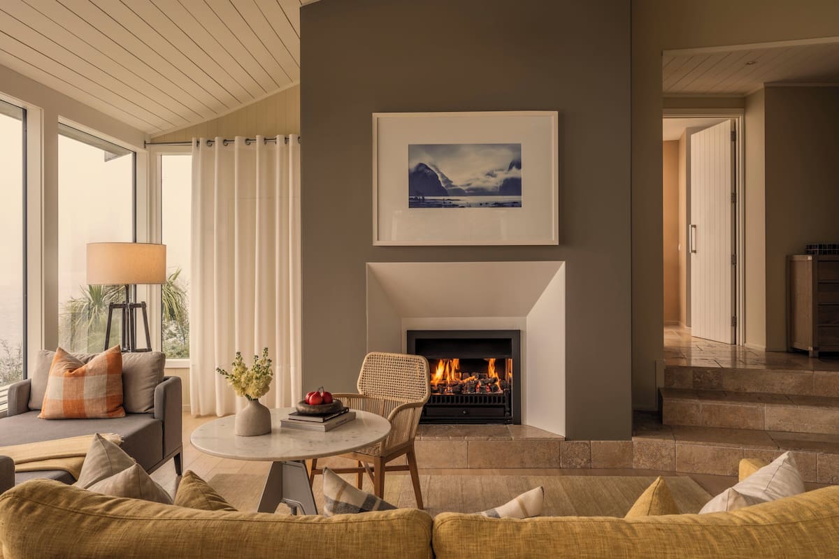 A modern living room with a fireplace, a sofa, a coffee table, and a view of the outdoors.