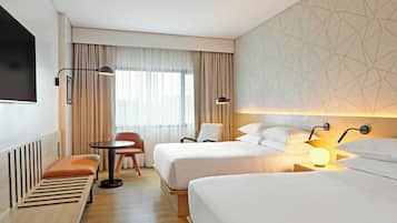 A hotel room with two beds, a desk, a chair, a TV, and a window with curtains.
