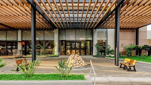 A modern building entrance with a wooden pergola, a stone sculpture, and outdoor seating. - Sheraton Asuncion Hotel (Asuncion)