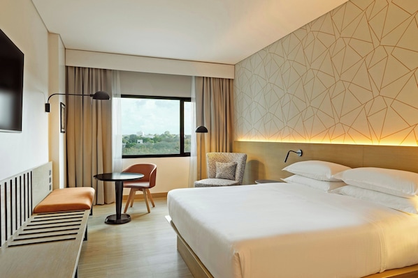 Una habitación de hotel con cama, escritorio, silla y ventana con cortinas.