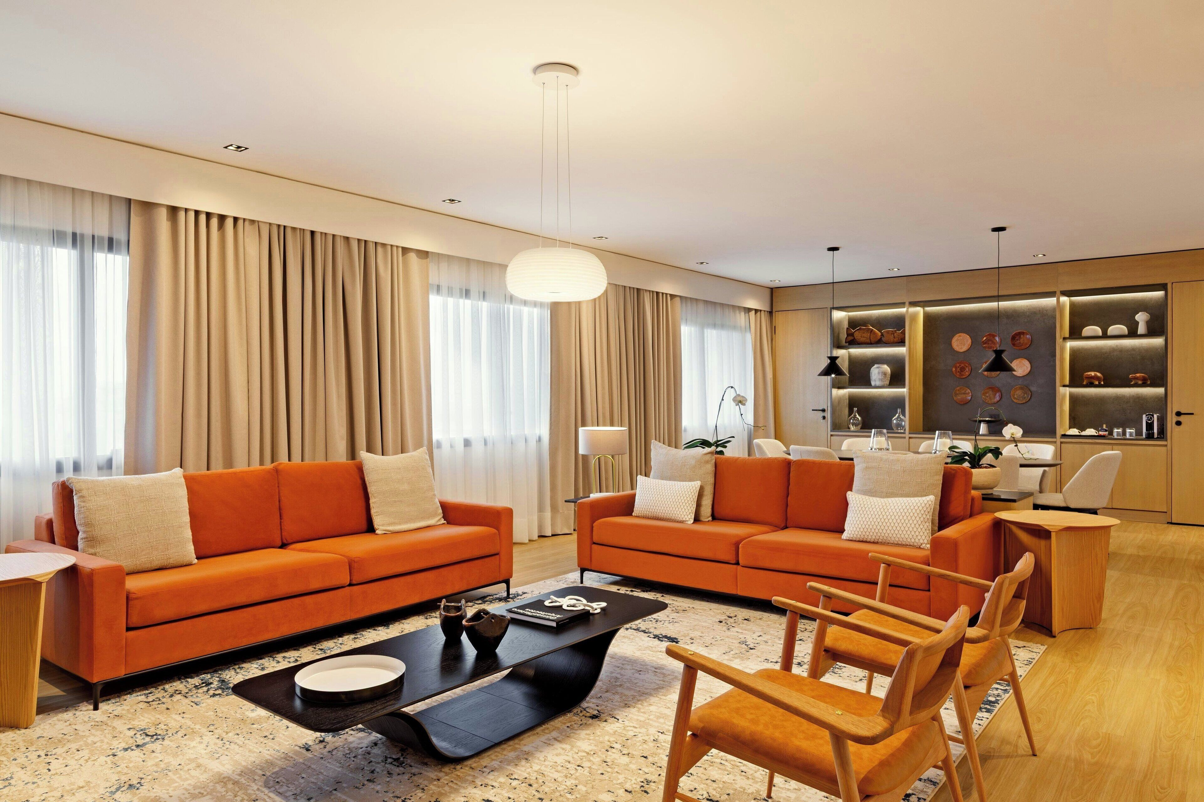 A modern living room with two orange sofas, a coffee table, and wooden chairs.