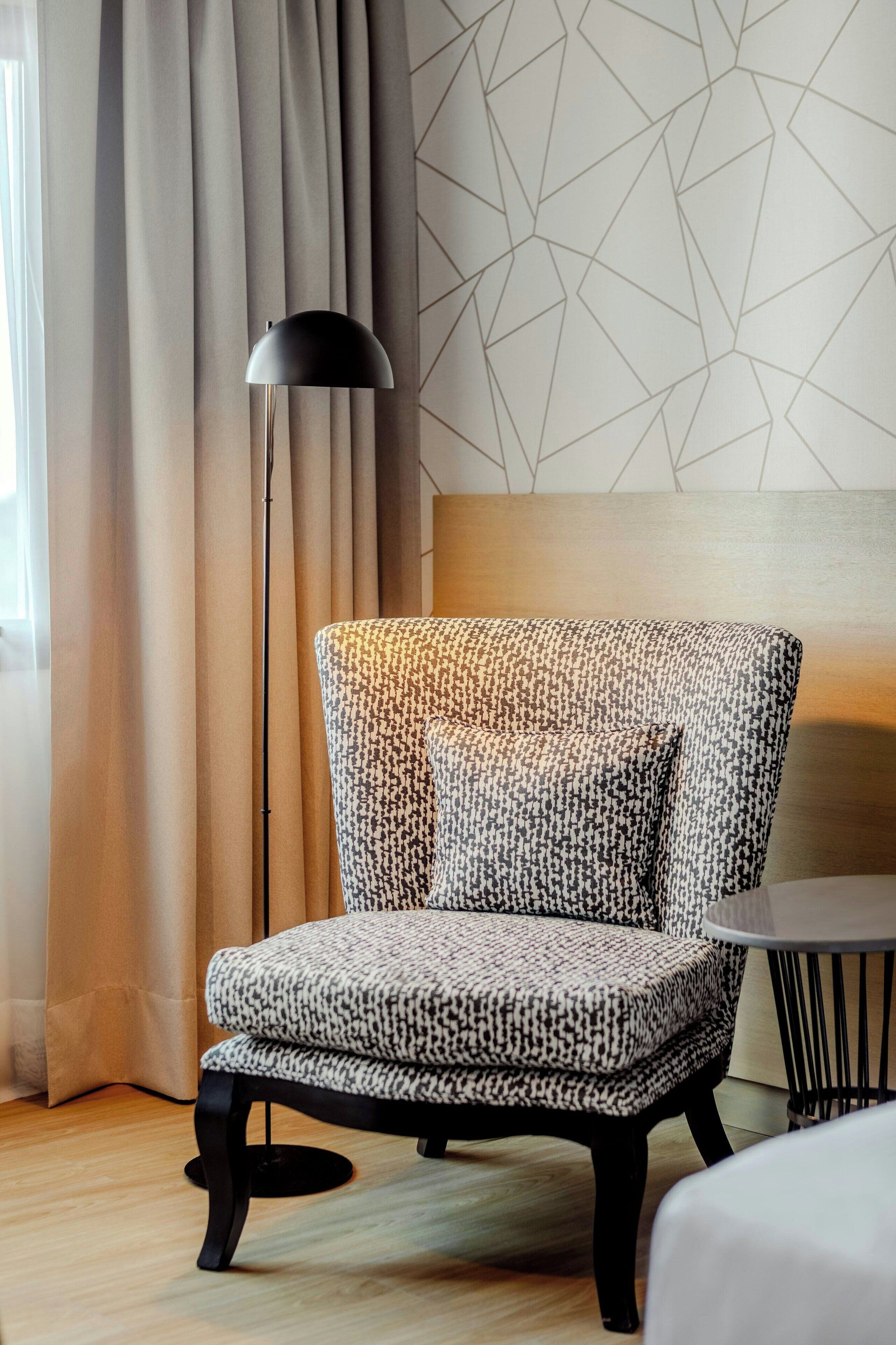 A modern room with a patterned armchair, a floor lamp, and a geometric wall design.