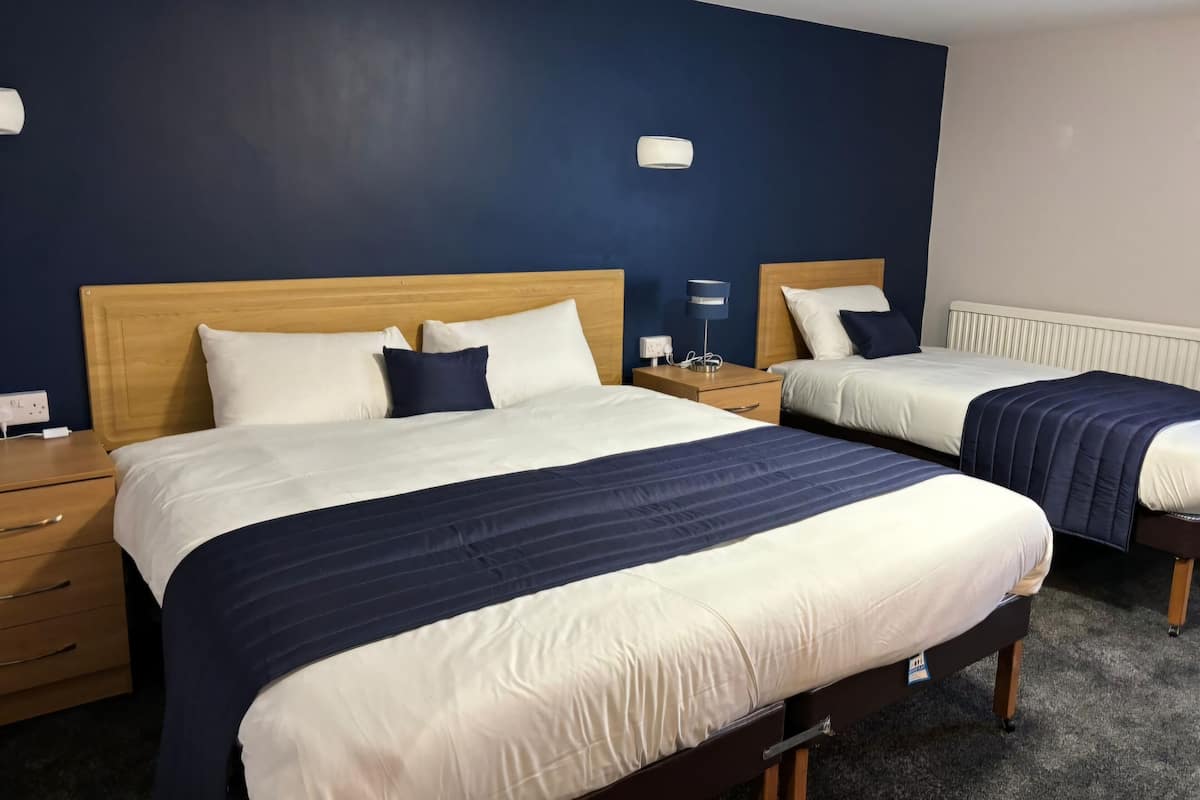 A hotel room with two beds, each with a wooden headboard, white and navy bedding, and a bedside table with a lamp.