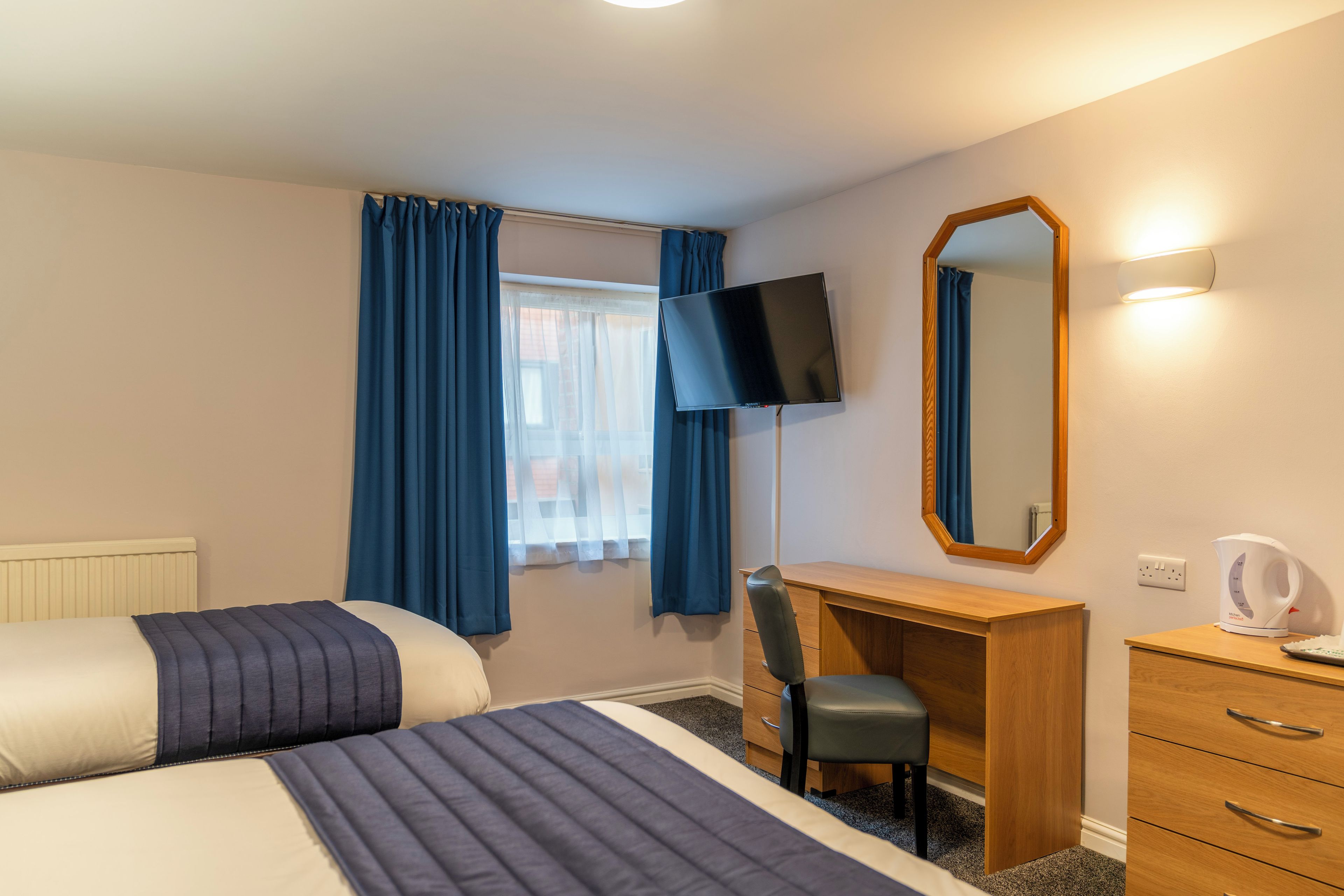Een hotelkamer met twee bedden, een bureau, een stoel, een flatscreen televisie, een spiegel en een waterkoker.