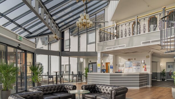 A spacious lobby with leather sofas, a reception desk, and a glass ceiling. - Britannia Hotel Wigan (Wigan)