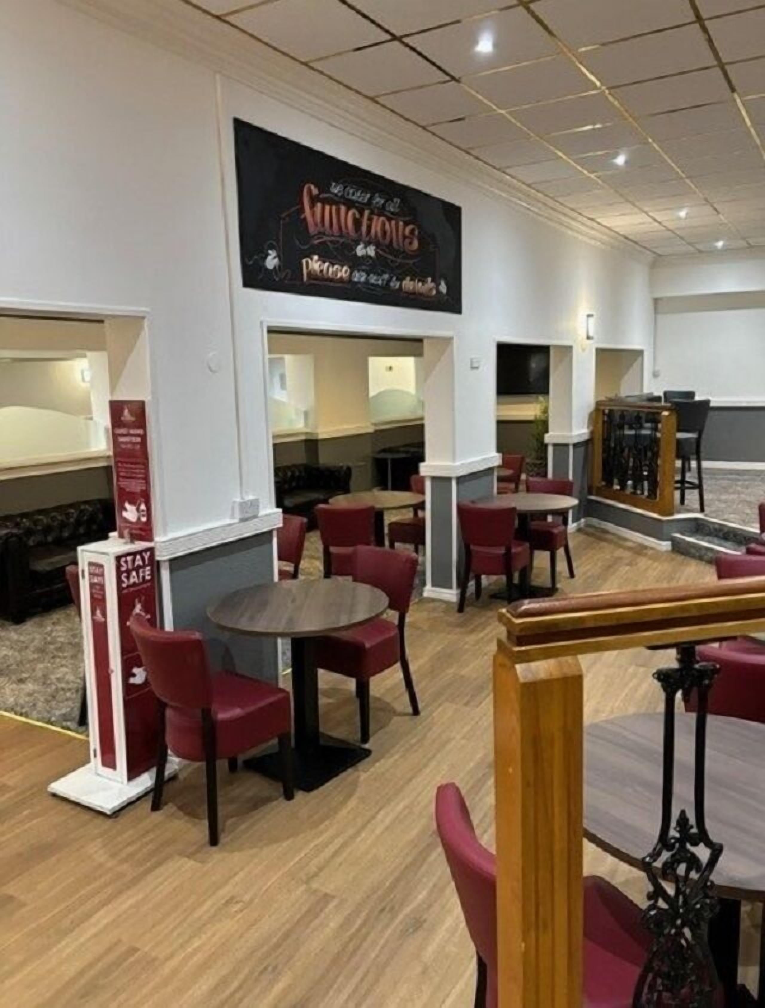 A restaurant with red chairs and tables, a sign above the entrance, and a 'STAY SAFE' sign on the wall.
