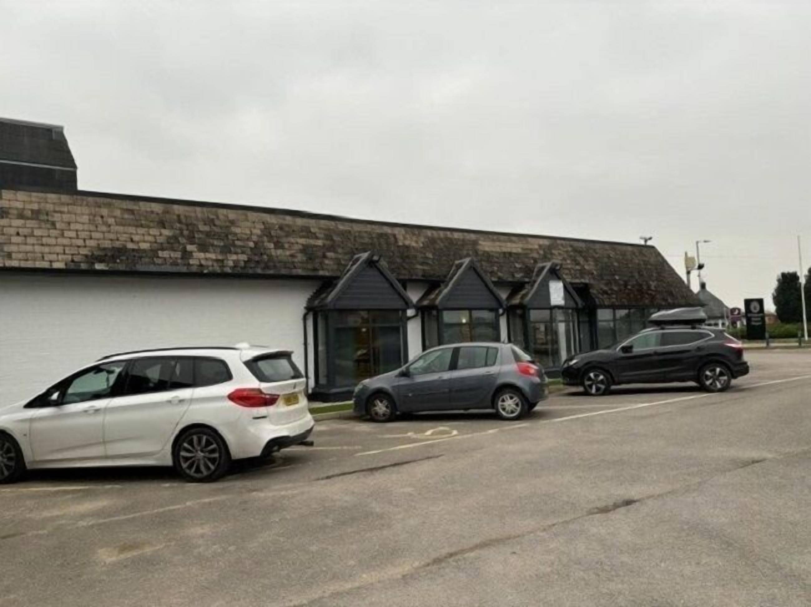 En parkeringsplads med tre biler parkeret foran en bygning med en stenfacade og et saddeltag.